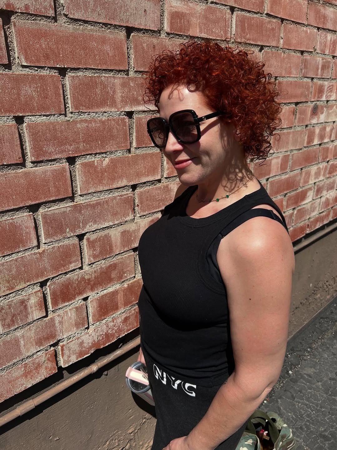 Bold crimson curly hair, editorial profile against brick